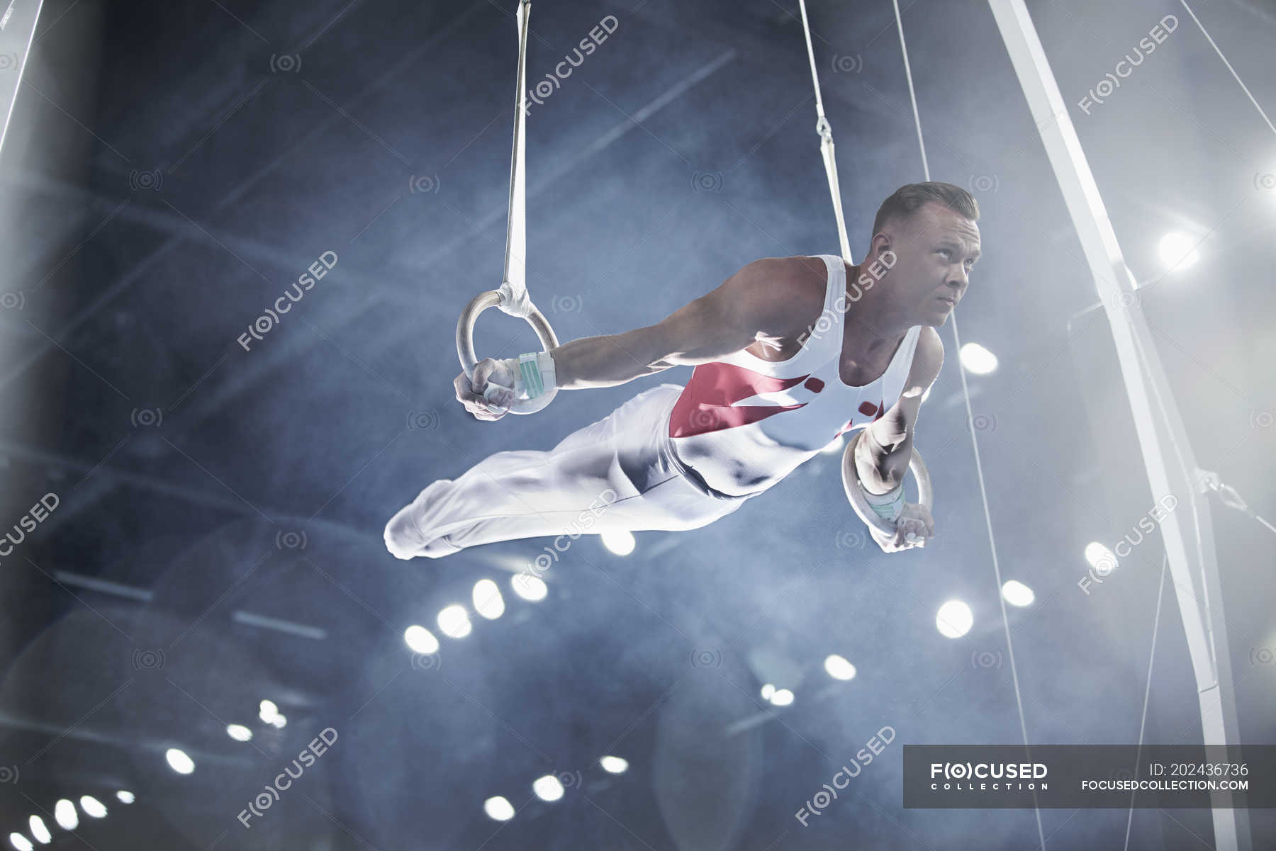 Male gymnast performing on gymnastics rings in arena — challenge