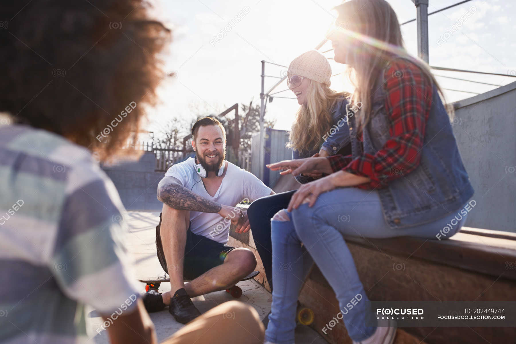 Friends with skateboards hanging out and talking at sunny skate park ...