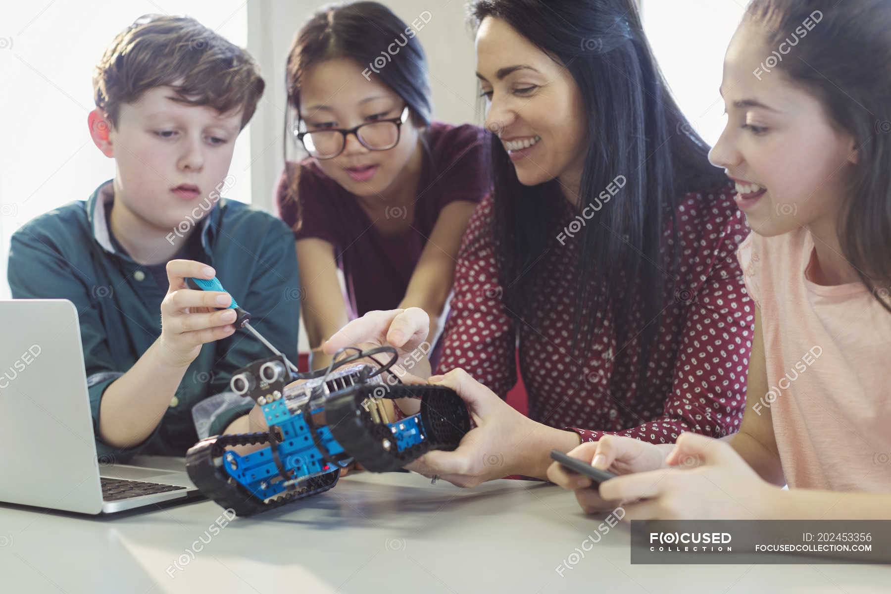 Female teacher and students programming and assembling robotics in ...