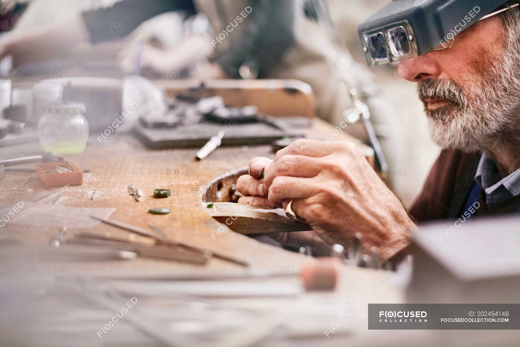 Male jeweler using headband magnifier making jewelry in workshop ...