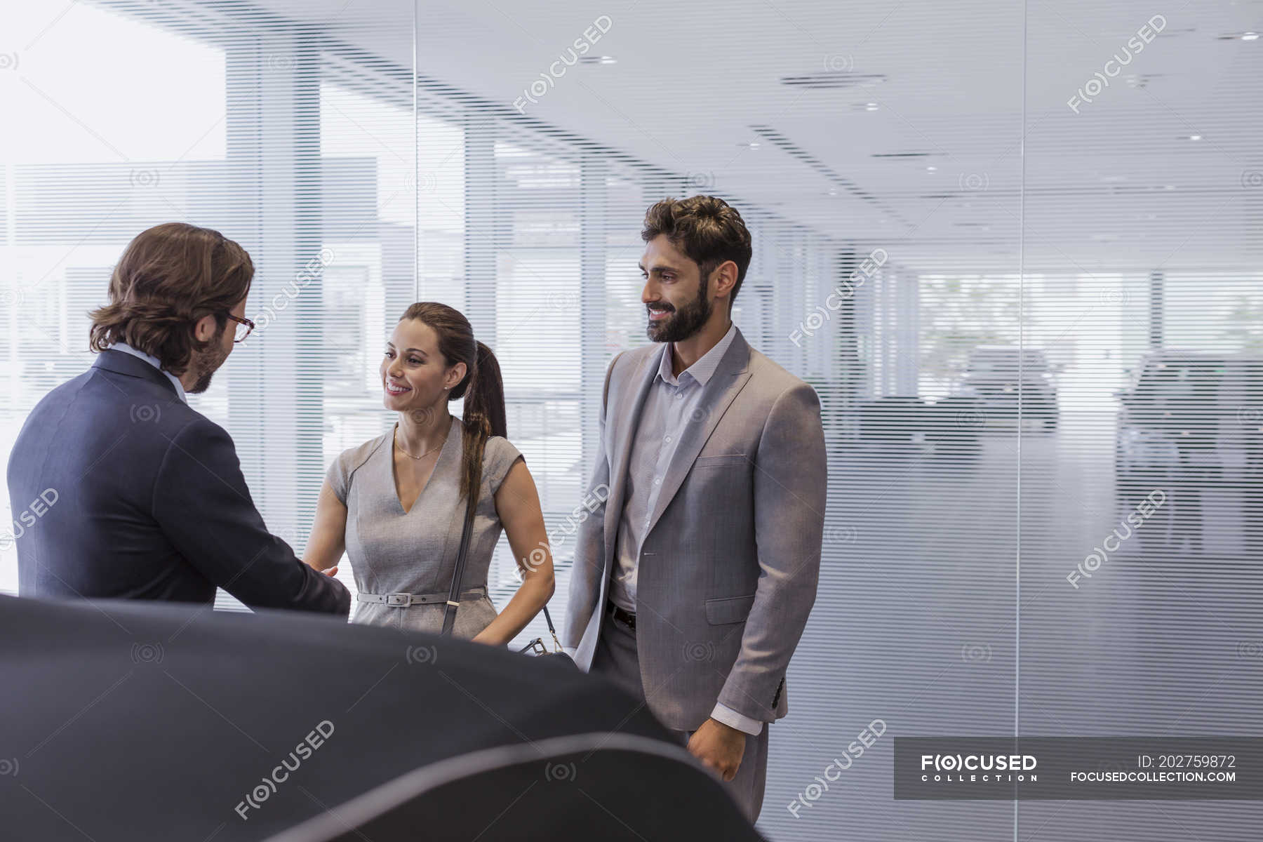 Car Salesman Greeting Couple Customers In Car Dealership Showroom Heterosexual Couple Closing The Deal Stock Photo