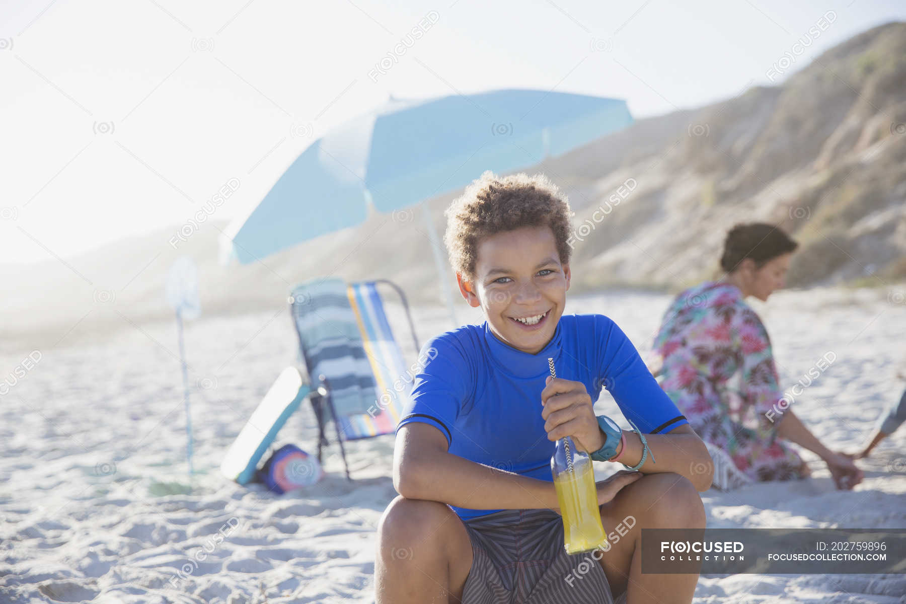 Portrait smiling, confident boy drinking juice on summer sunny beach ...