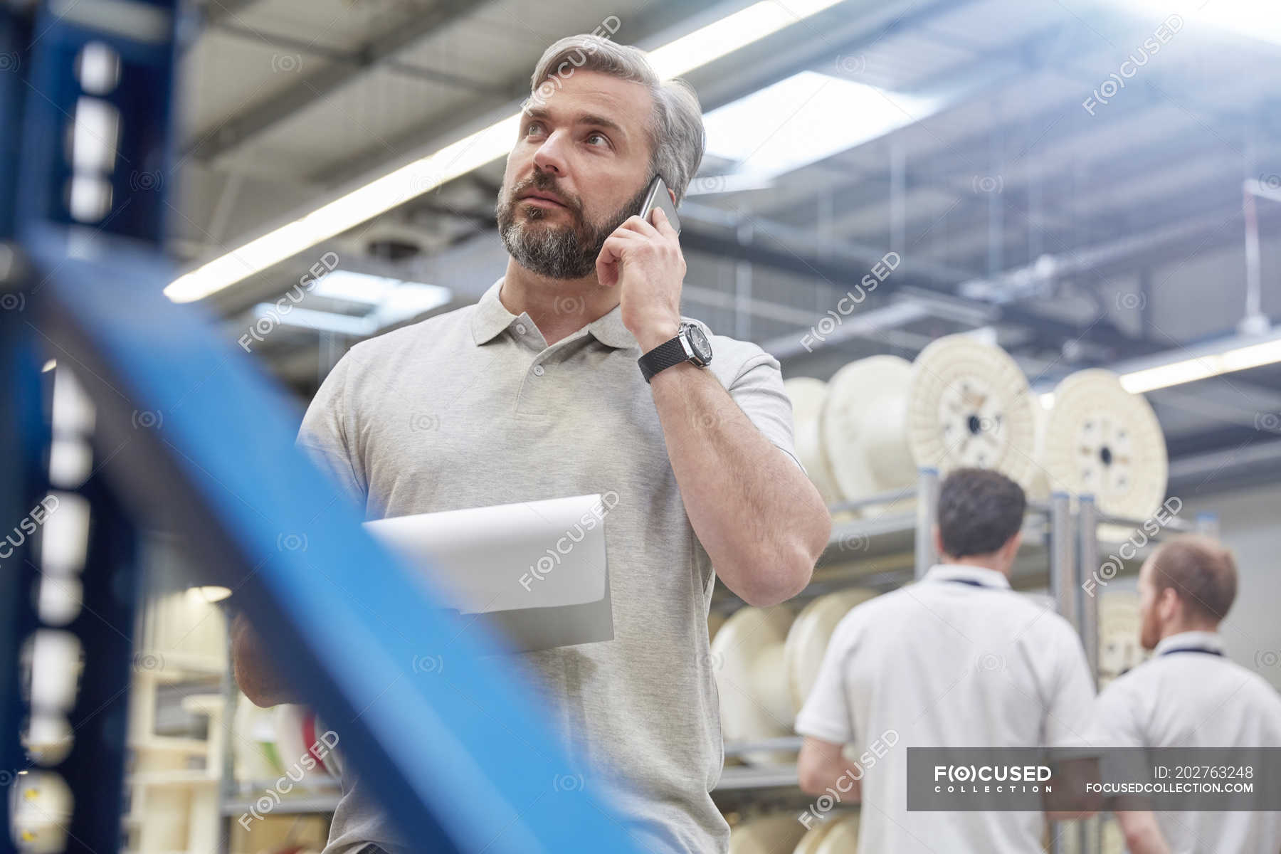 Male supervisor with clipboard talking on cell phone in fiber optics ...