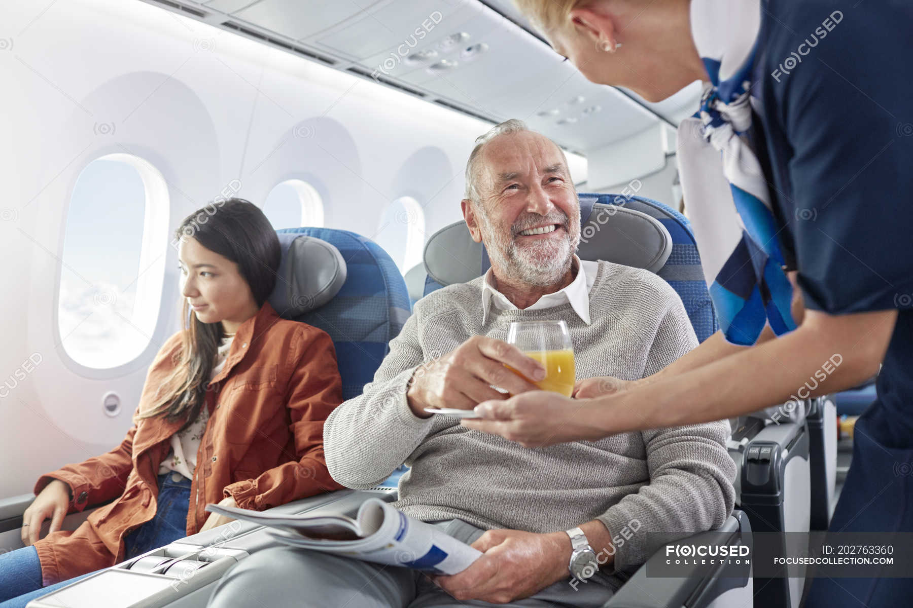 Flight attendant serving orange juice to man on airplane — senior adult ...