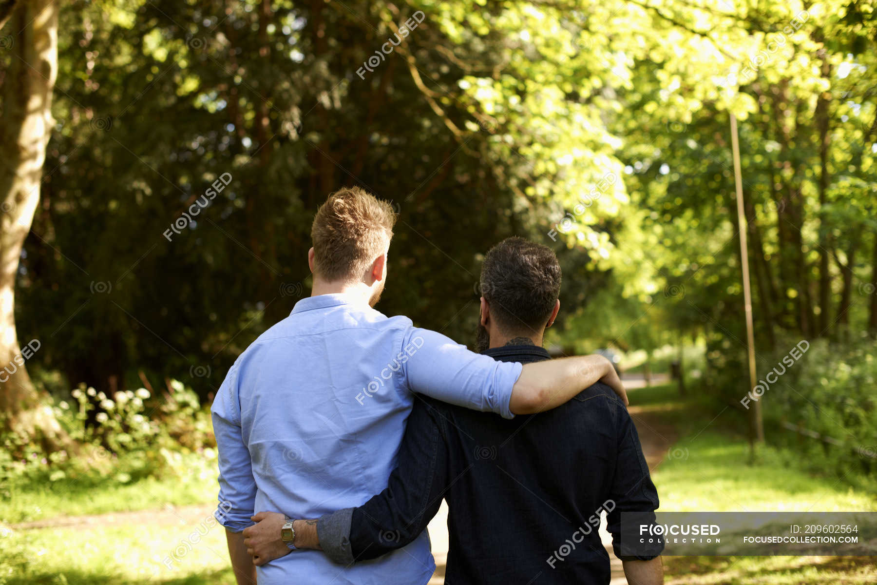 Affectionate gay couple hugging, walking in sunny park — gay nature - Stock | #209602564
