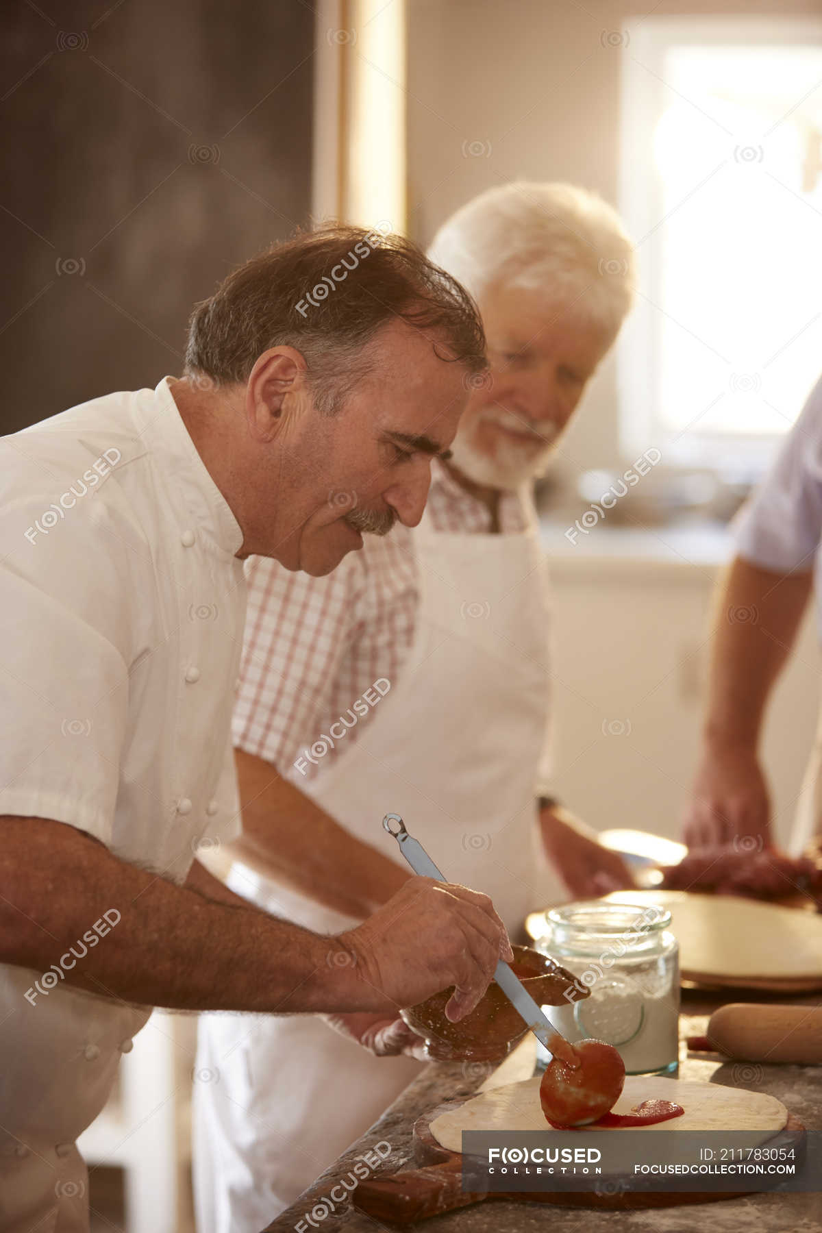 Chef spreading marinara sauce on pizza dough in cooking class