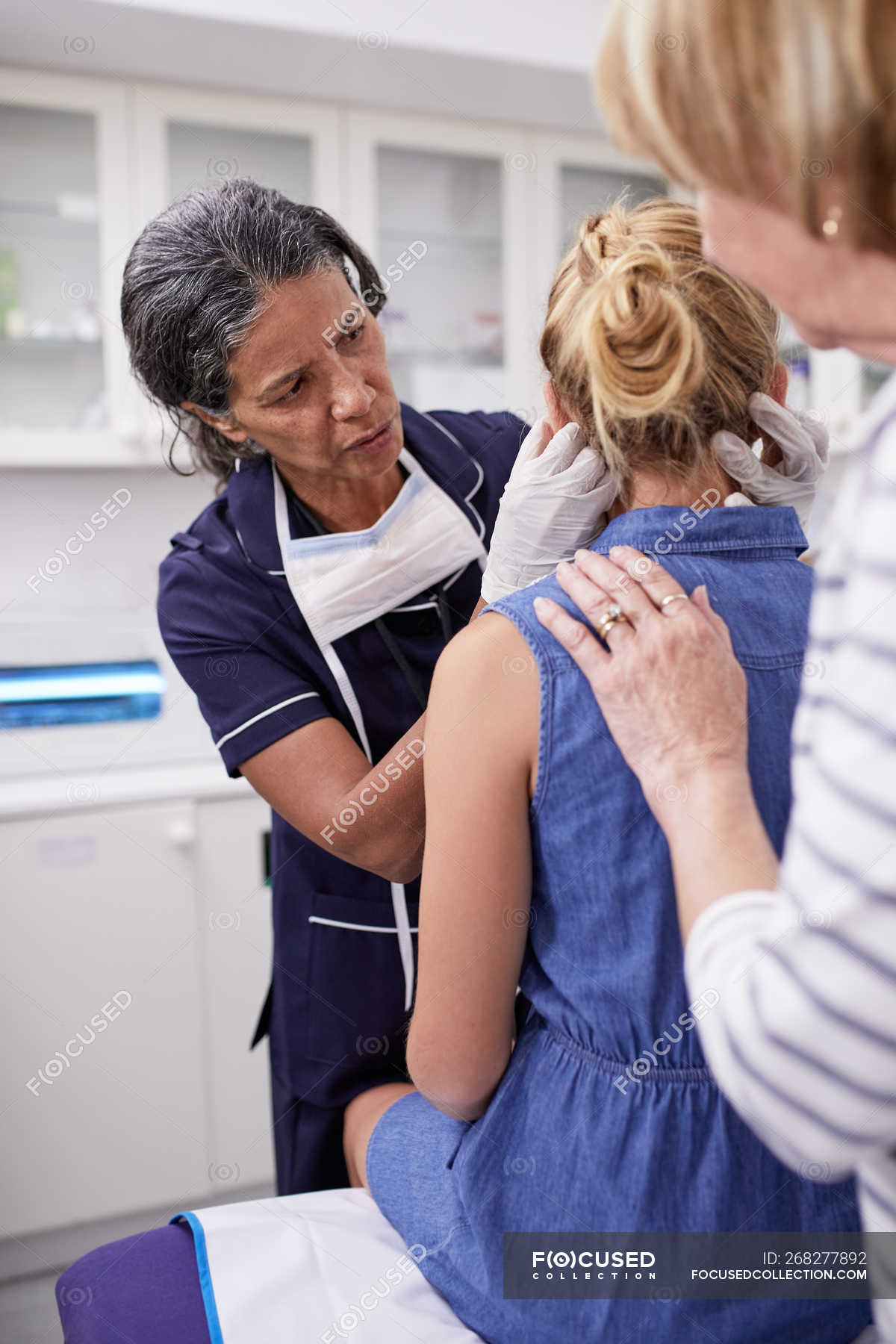 Female Doctor Examining Girl Patient In Examination Room Rubber Gloves Looking Down Stock