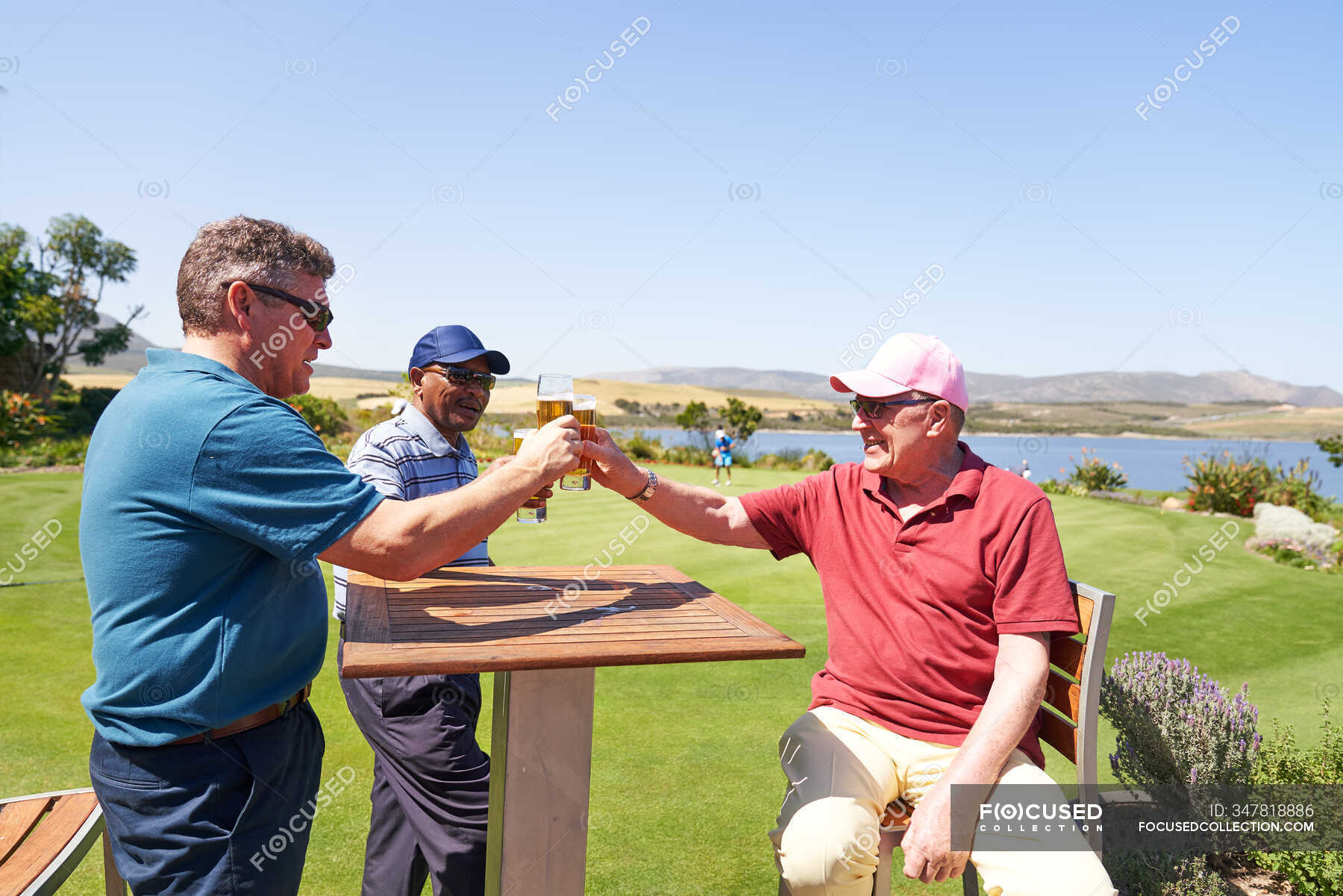 Mature male golfers drinking beer on sunny golf clubhouse patio ...