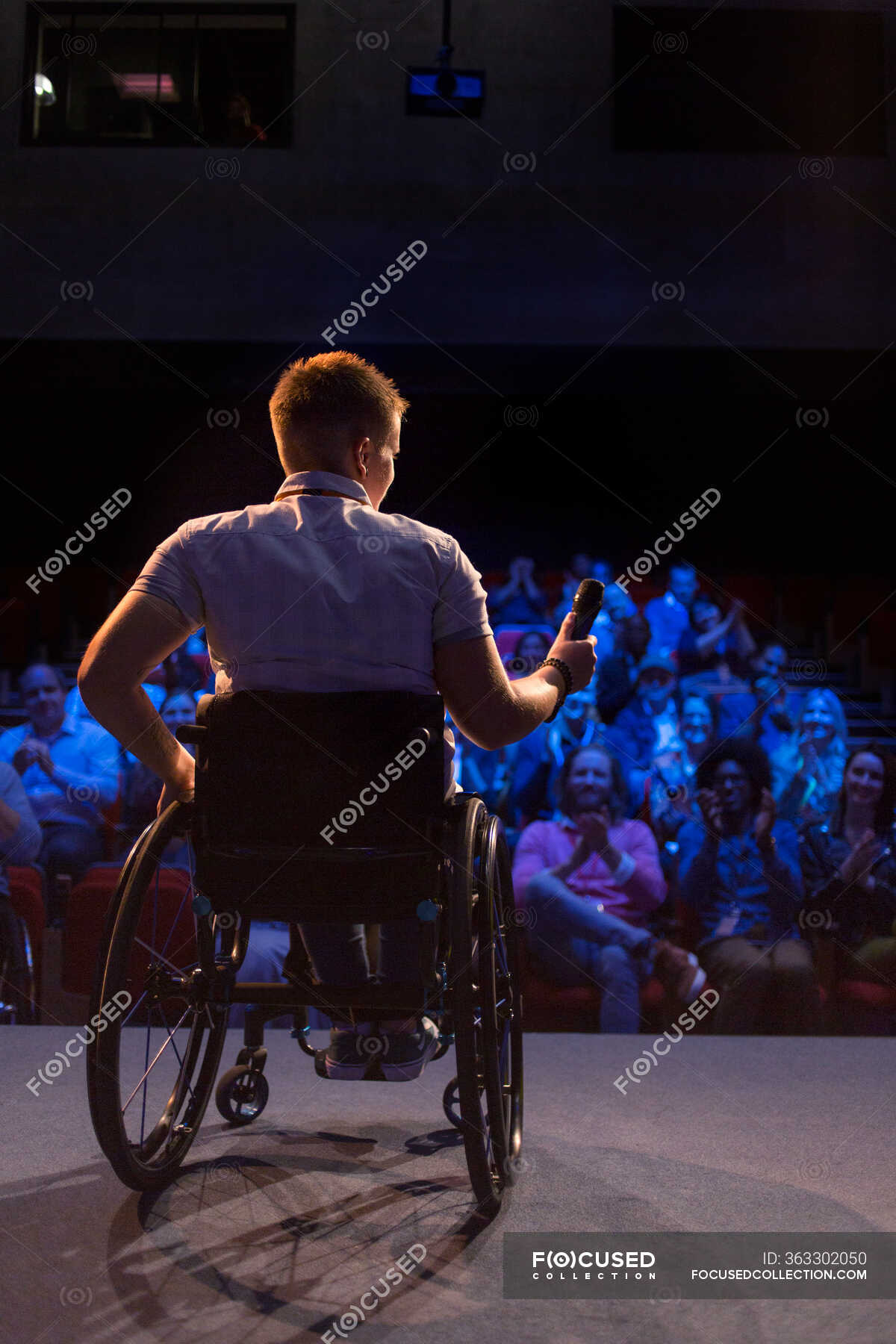 Female speaker with microphone in wheelchair on stage — disabled