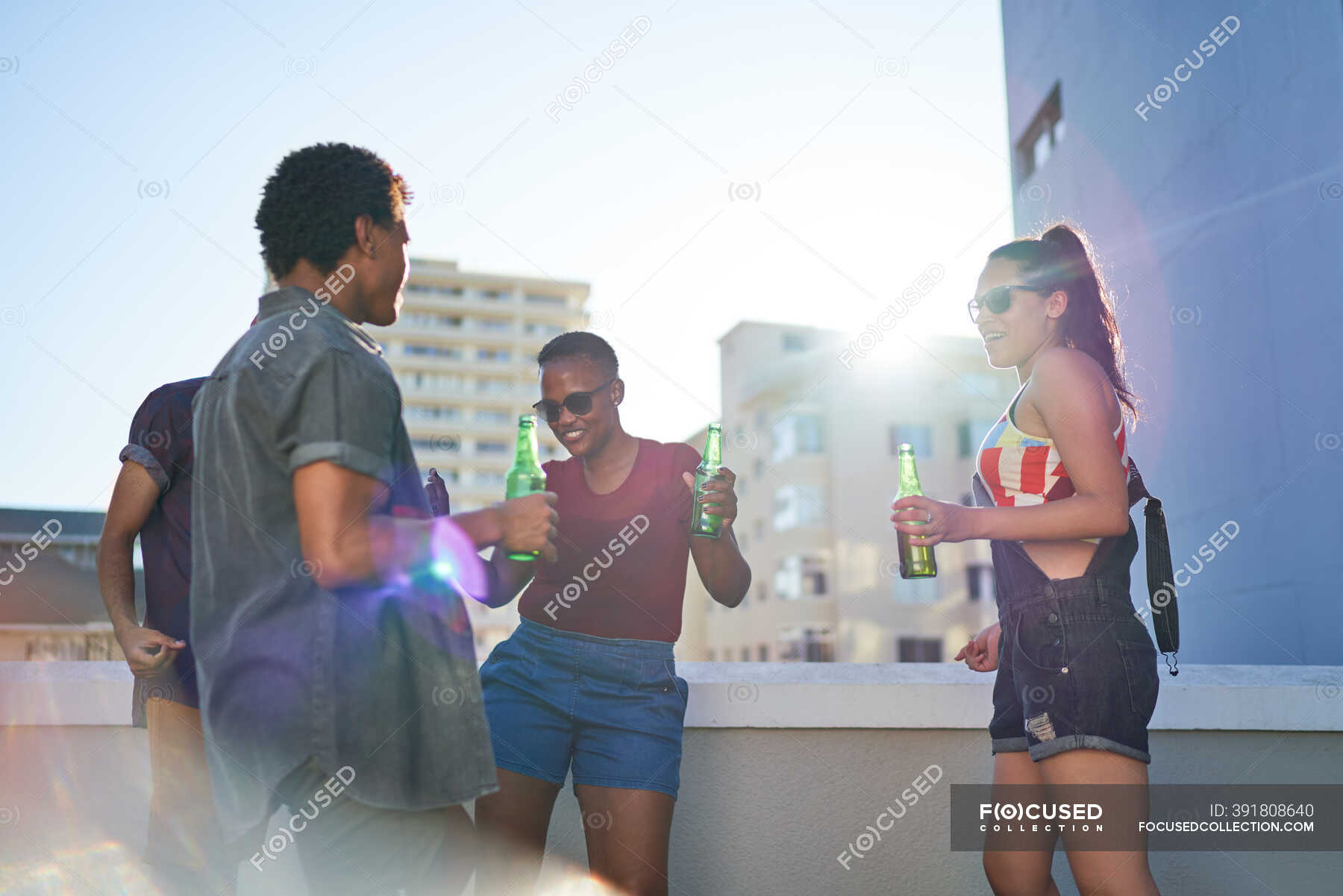 Young friends dancing and drinking beer on sunny urban rooftop balcony ...