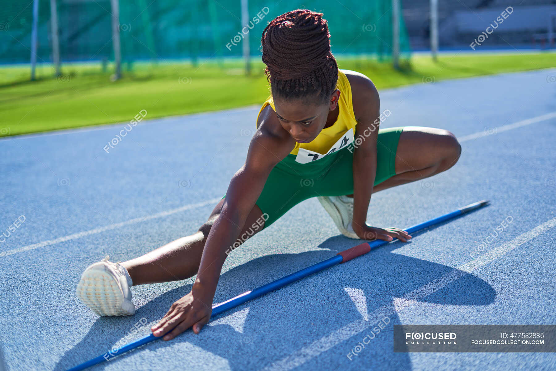Female track and field athlete with javelin stretching on sunny track