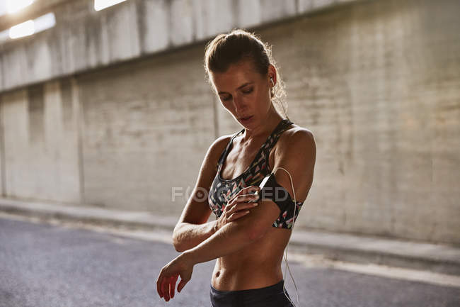 Fitte Läuferin im Sport-BH mit MP3-Player-Armband und Kopfhörer auf der Straße — Stockfoto