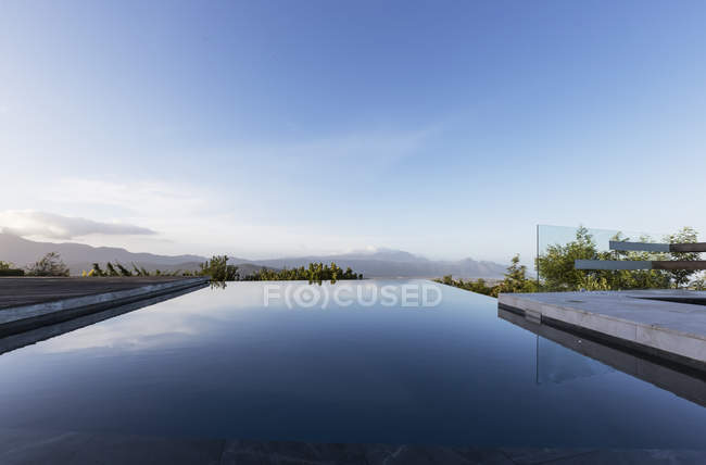 Tranquil luxury infinity pool with mountain view below blue sky — Stock Photo