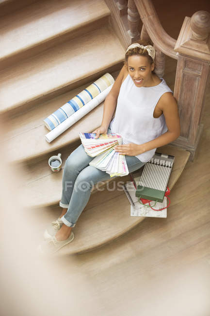 Mujer sentada en escaleras mirando a través de muestras de color - foto de stock