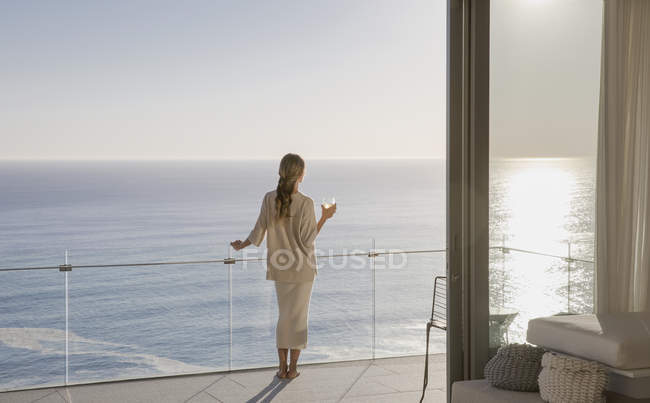 Mulher em pé na varanda de luxo ensolarado com vista para o mar — Fotografia de Stock