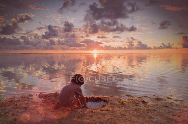 Niño jugando en arena mojada en la playa tranquila puesta de sol - foto de stock