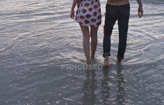 Jeune couple marchant dans le surf océanique — Photo de stock