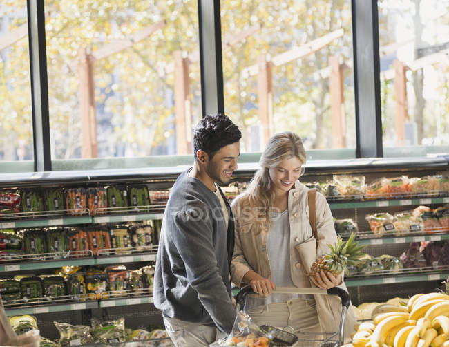 Smiling young couple grocery shopping, holding pineapple in market — Stock Photo