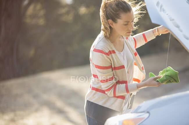 Donna che controlla l'olio sotto il cofano dell'automobile a bordo strada — Foto stock
