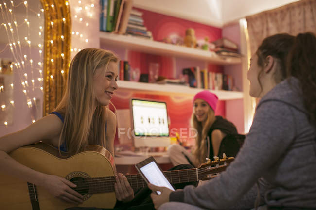 Дівчата-підлітки грають на гітарі і використовують цифровий планшет у спальні — стокове фото