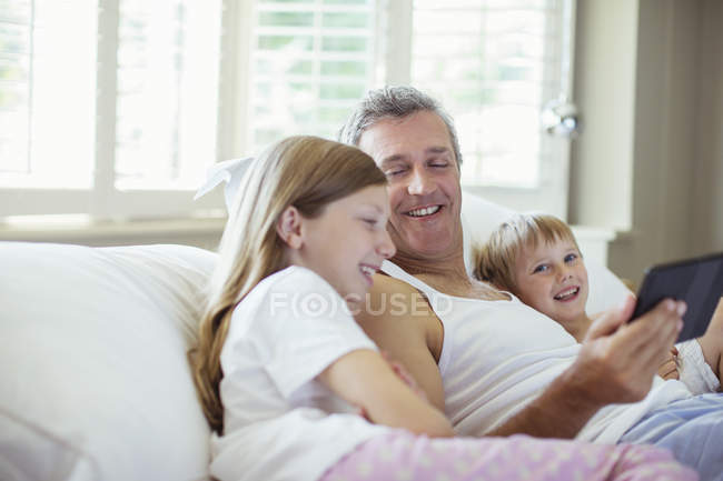 Pai e crianças usando tablet digital na cama — Fotografia de Stock
