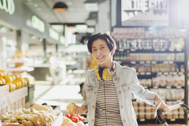 Retrato sonriente, mujer joven confiada con auriculares compras de comestibles en el mercado - foto de stock