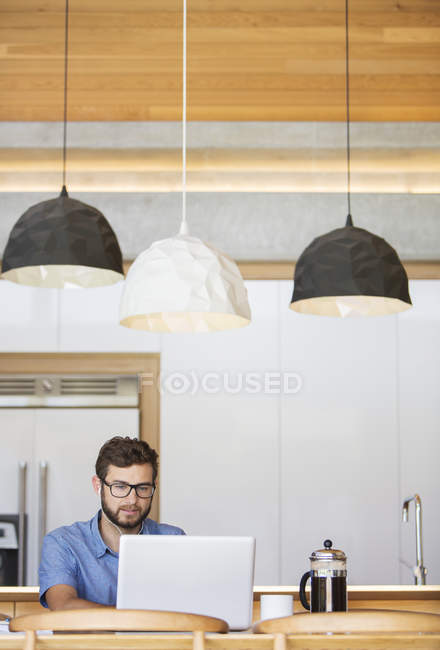 Homem usando laptop sob luzes pendentes na cozinha — Fotografia de Stock