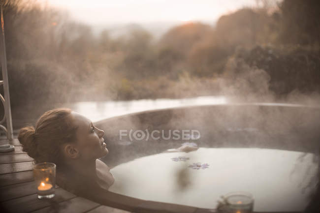 Serene woman soaking in steaming hot tub with autumn tree view — Stock Photo