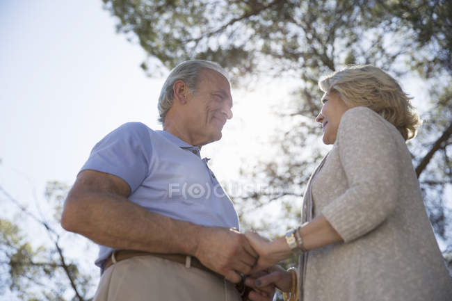 Счастливая пожилая пара, держащаяся за руки под деревом — стоковое фото