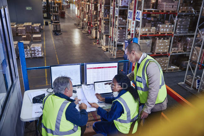 Managers at laptop and computers discussing paperwork in distribution warehouse — Stock Photo