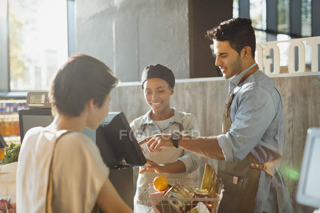 Cashiers helping customer at grocery store market checkout — Stock Photo
