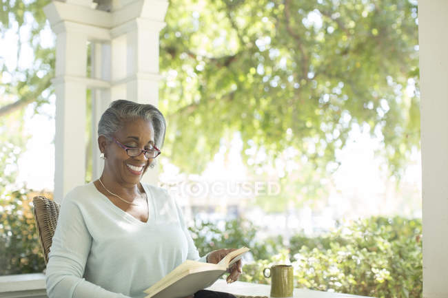 Happy senior woman reading book on porch — Stock Photo