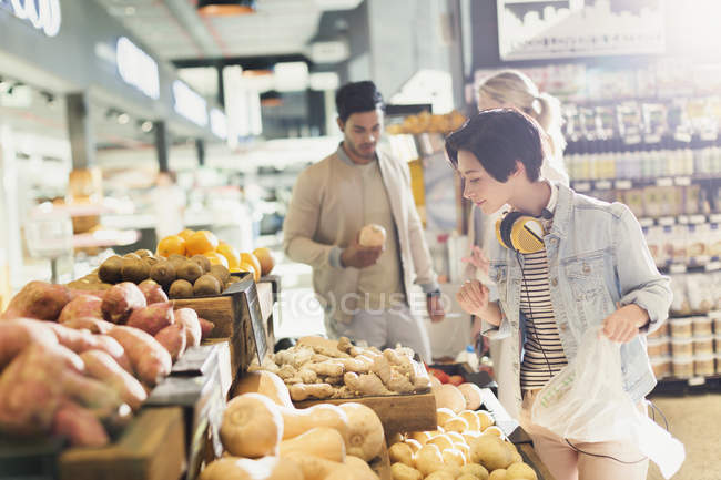 Молодая женщина с наушниками продуктовый магазин, просмотр продукции на рынке — стоковое фото