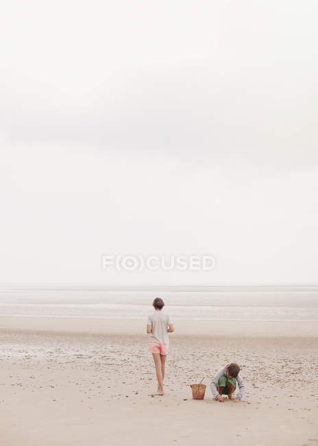 Brother and sister playing in sand on overcast summer beach — Stock Photo