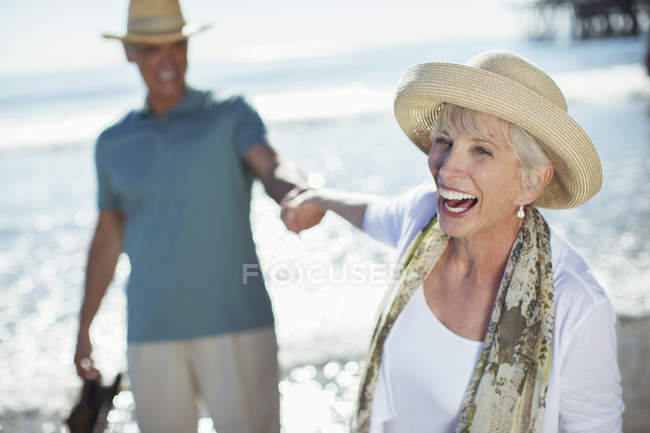 Couple sénior enthousiaste tenant la main sur la plage ensoleillée — Photo de stock