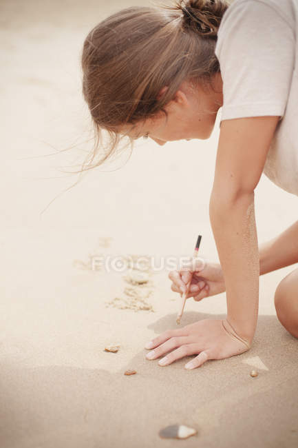 Adolescente avec bâton écrit dans le sable sur la plage d'été — Photo de stock