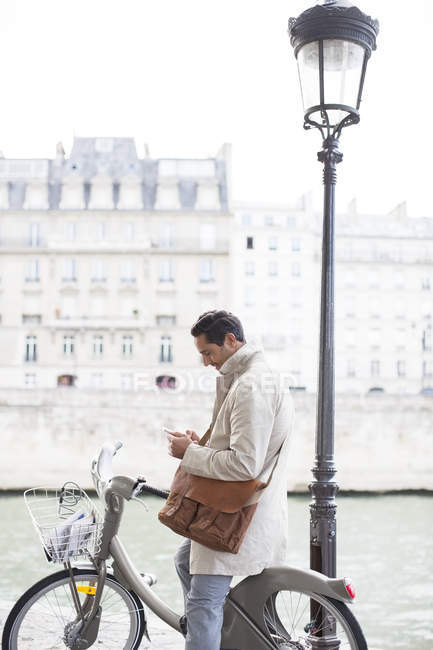 Бизнесмен, использующий сотовый телефон на велосипеде вдоль реки Сены, Париж, Франция — стоковое фото