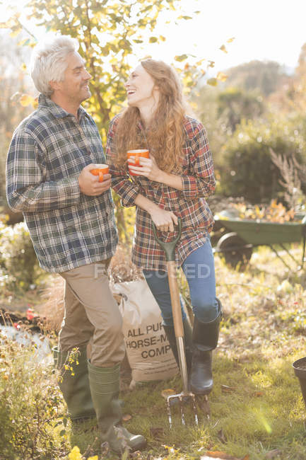 Pareja riendo disfrutando de café descanso jardinería soleado jardín de otoño - foto de stock