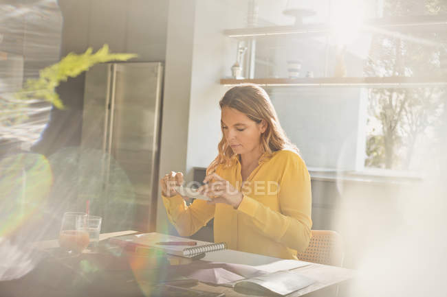 Femme avec appareil photo téléphone photographie art à la table de cuisine ensoleillée — Photo de stock