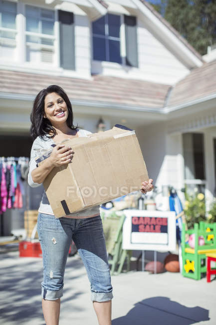 Porträt einer lächelnden Frau mit Schachtel beim Garagenverkauf — Stockfoto