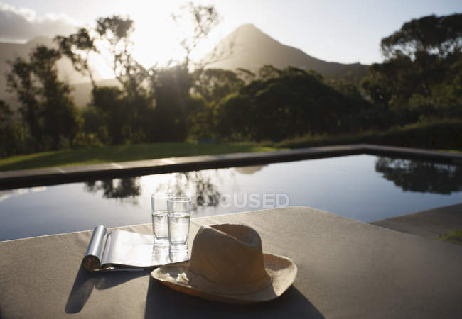 Chapéu de sol, copos de água e revista sobre espreguiçadeiras à beira da piscina — Fotografia de Stock