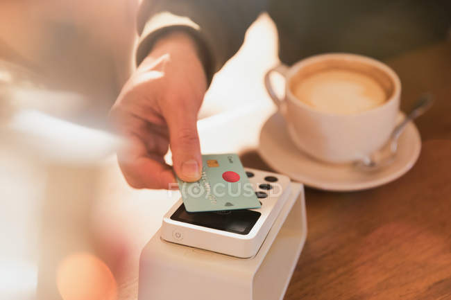 Fechar o homem pagando por cappuccino com cartão de crédito pagamento sem contato no café — Fotografia de Stock