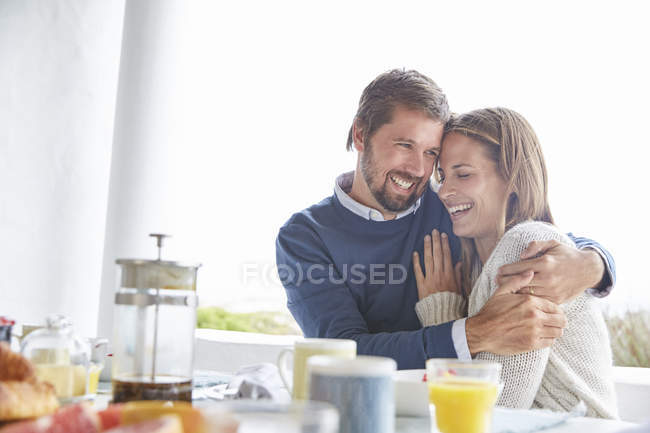 Smiling affectionate couple hugging at patio breakfast table — Stock Photo