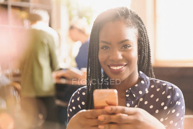 Портрет посміхаючись африканською жінкою текстові повідомлення з мобільного телефону в кафе — стокове фото