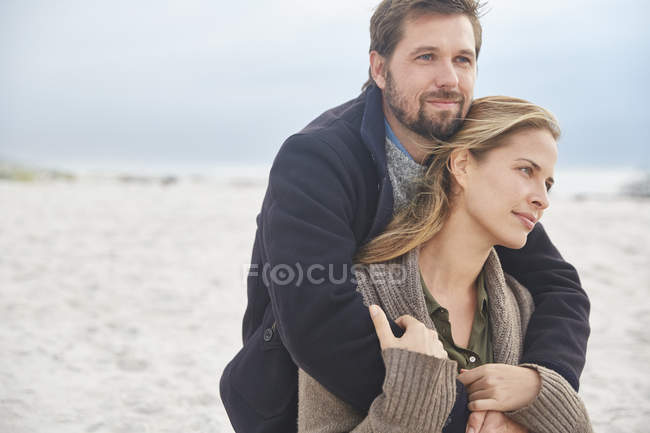 Serena pareja cariñosa abrazándose en la playa de invierno - foto de stock
