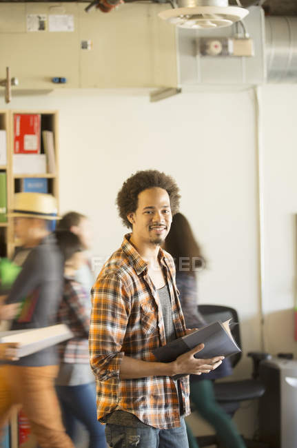 Portrait of confident casual businessman in office with co-workers passing by in background — Stock Photo