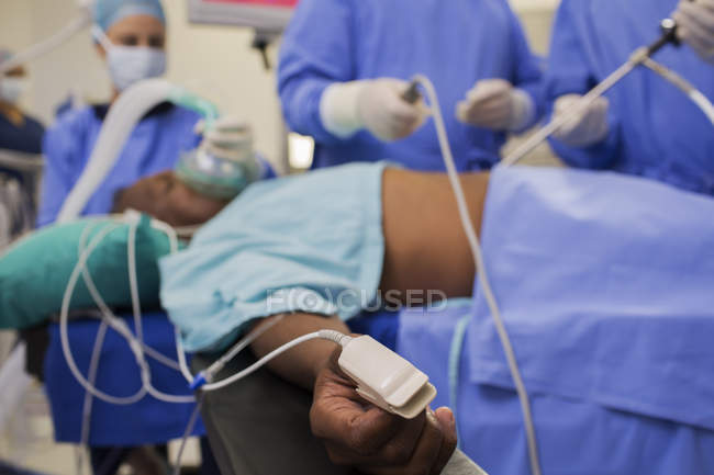 Médecins pratiquant une chirurgie laparoscopique, patient avec oxymètre de pouls sur le doigt — Photo de stock