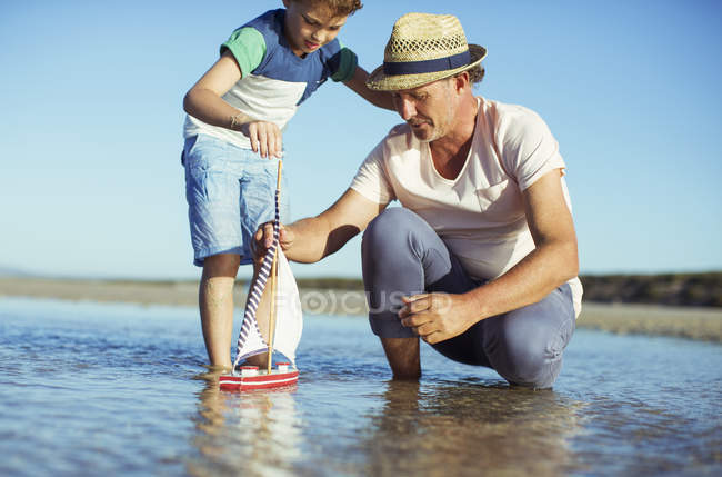 Avô e neto brincando com barco de brinquedo na água — Fotografia de Stock