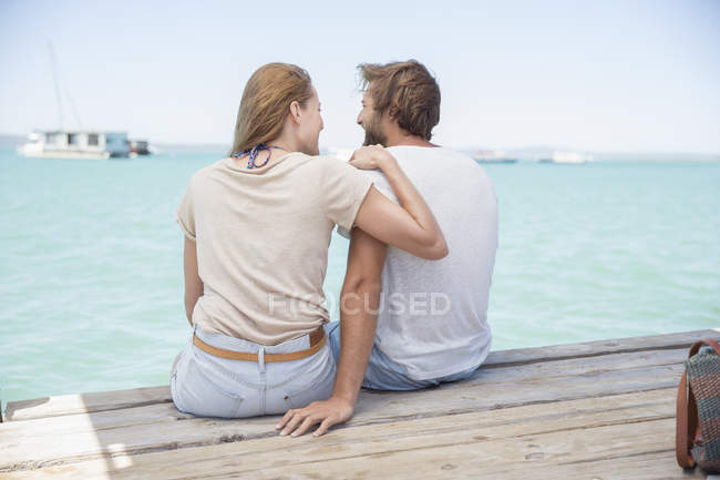 Couple sitting on edge of wooden dock together — Stock Photo