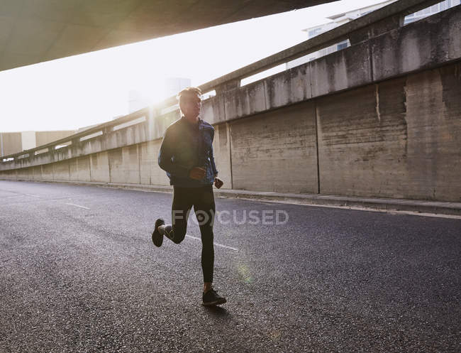 Male runner running on urban street into tunnel — Stock Photo